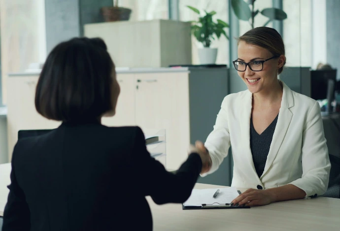Two women shaking hands across a desk